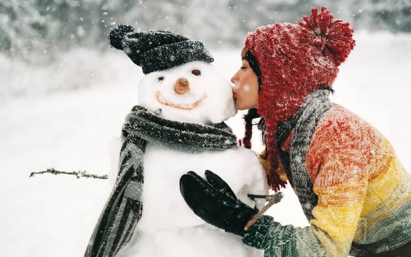 девушка целует снеговика зимой на снегу обои для рабочего стола