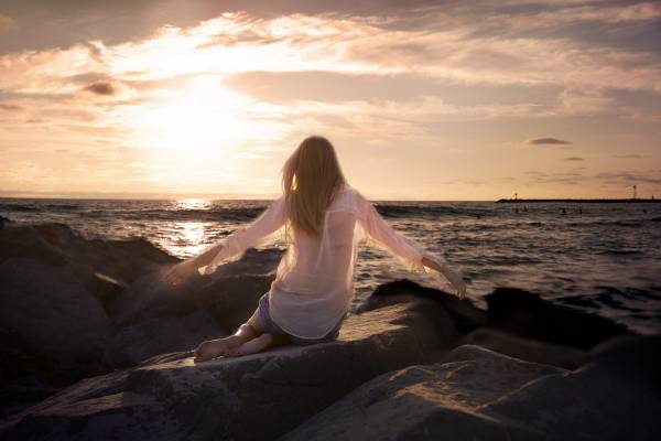 девушка у моря на закате солнца сидит на камнях обои для рабочего стола